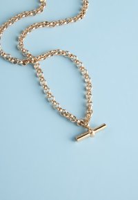 Gold chain necklace with a T-bar clasp laid out on a light blue surface.