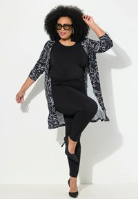 Leggings neri aderenti abbinati a un top nero e a un lungo cardigan a righe bianche e nere. La modella indossa tacchi alti neri e occhiali da sole.