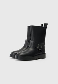 Μαύρες δερμάτινες μποτάκες μέχρι τον αστράγαλο με στρογγυλή μύτη, επίπεδη σόλα και ατσάλινη αγκράφα στο πλάι. Διαθέτουν γλωττίδες για εύκολη χρήση.