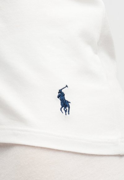 Λευκό ύφασμα με μικρό κεντημένο λογότυπο σε ναυτικό μπλε που δείχνει έναν παίκτη πόλο πάνω σε άλογο κρατώντας ανυψωμένη ρακέτα.