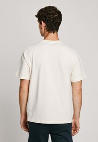 T-shirt in cotone a maniche corte di colore crema chiaro, con scollo rotondo, taglio dritto e design minimalista; texture morbida e senza loghi visibili.