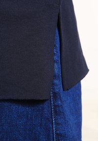 Maglietta di cotone navy con uno spacco laterale, sovrapposta a una gonna in denim blu dalle texture. Presenta un design pulito e una finitura morbida.