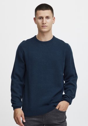 Navy blue knitted sweater with a round neckline, ribbed cuffs, and hem. The fabric is textured and has a casual fit. Grey pants visible.