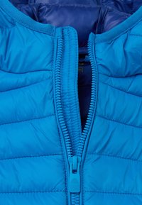 Chaqueta acolchada azul con cremallera frontal completa, diseño acolchado texturizado y un forro interior suave. Color brillante con herrajes a juego.