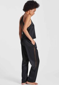 Ensemble de nuit en satin noir comprenant un top court avec un dos original et des accents en dentelle, associé à un pantalon ample avec des poches latérales.