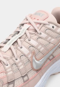 Gaiši rozā Nike sporta apavi ar sieta paneļiem, sudraba swoosh logotipu un krusteniski izsietām auklām ar "Powertrain Series" uzlīmi.