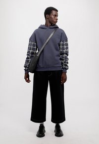 Námornícka mikina s vzorovanými rukávmi, spárovaná s čiernymi širokými nohavicami a čiernymi topánkami. Čierna crossbody taška dotvára outfit.