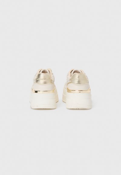 Zapatillas tipo plataforma en beige con detalles metálicos dorados, parte superior texturizada y suelas lisas. Presentan una marca en el talón y un collarín acolchado.