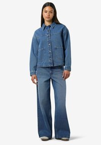 Chaqueta de mezclilla y pantalones de pierna ancha en azul medio. La chaqueta cuenta con dos bolsillos delanteros, cierre de botones y cuello. Tejido suave y texturizado.