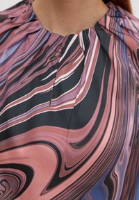 Mehrfarbige Bluse mit spiralförmigen Mustern in Rosa, Lila und Schwarz. Weicher Stoff mit gefaltetem Kragen.