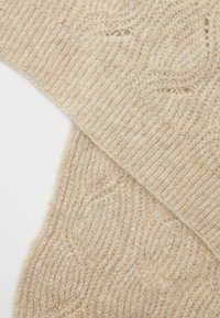 Sweter dzianinowy w jasnym beżu, z prążkowanymi mankietami i fakturowanym wzorem z falistymi motywami na całym ciele. Miękki, puszysty materiał.
