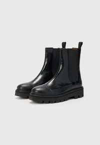 Bottines Chelsea en cuir noir avec une finition brillante, panneaux latéraux élastiques, bout rond et semelle en caoutchouc épaisse dotée d'un motif de sculpture profond.