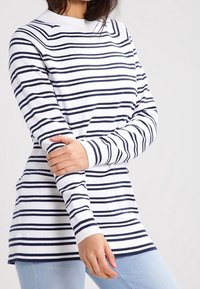 Pull rayé blanc avec des rayures horizontales bleu marine, poignets côtelés et col montant, superposé à un jean bleu clair.