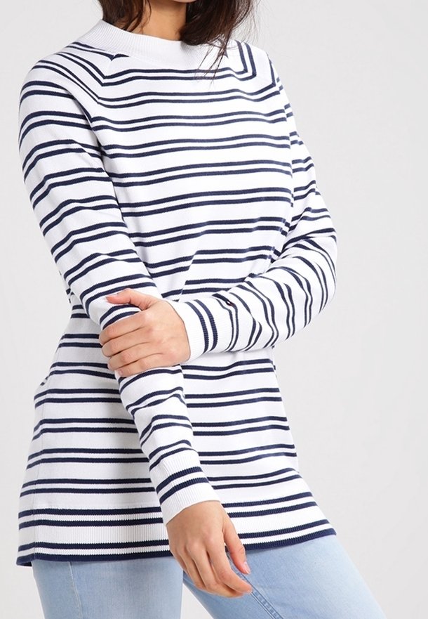 Pull rayé blanc avec des rayures horizontales bleu marine, poignets côtelés et col montant, superposé à un jean bleu clair.