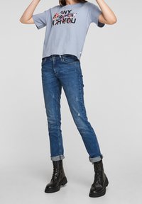 Camiseta de manga corta azul claro con un gráfico floral; combinada con unos jeans skinny desgastados de color azul oscuro; botas de combate negras con cordones.