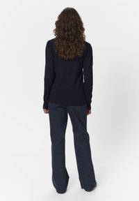 Jūras spēku adīts džemperis ar garām piedurknēm un ribotu apakšmalu, kombinēts ar tumšām, platiem biksēm. Tekstūrēta auduma, nedaudz brīvs piegriezums.