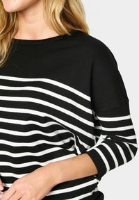 Juodai baltos juostelės sveturis su laisvu kirpimu, turintis trijų ketvirčių ilgio rankoves ir plačią iškirptę. Minkštas knit audinys.