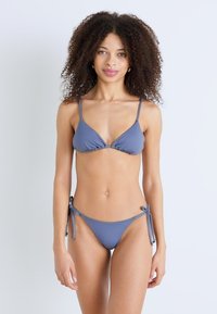 Niebieski zestaw bikini składający się z biustonosza w kształcie trójkąta oraz majtek z węzełkami po bokach, wykonany z gładkiego materiału, oferujący minimalne krycie oraz regulowane ramiączka.