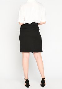 Svart blyertskjol med en åtsittande design, slät textur och sydda detaljer. Kompletterad med svarta klackar med ankelrem.