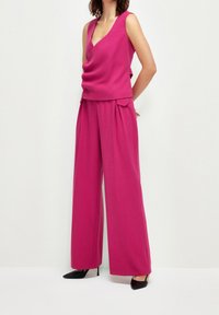 Fuchsiový třídílný outfit obsahující top bez rukávů s hlubokým výstřihem do V a široké kalhoty. Materiál má hladkou texturu a minimální detaily.