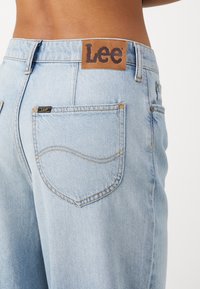 Vaaleansiniset farkut, joissa on ruskea nahkainen Lee-logopatchi vyötäröllä ja kaksi takataskua, joissa on hienovaraiset ompelut.