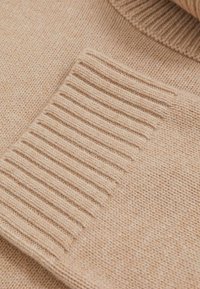 Beige gebreide trui met een zachte textuur. Heeft ribbel manchetten en kraag, wat zorgt voor een gezellige uitstraling met een gladde, gelijkmatige weving.