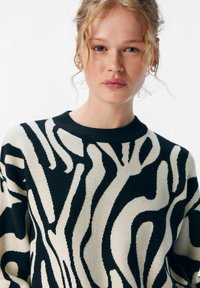 Schwarzer und cremefarbener Pullover mit abstraktem Muster, rundem Ausschnitt und strukturiertem Stoff. Verfügt über lange Ärmel und eine lockere Passform.