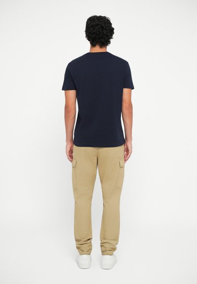 Marineblauwe T-shirt met korte mouwen en ronde hals, gedragen met beige cargo broek met zijzakken en witte sneakers. Minimalistisch ontwerp.