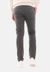 Pantaloni di cotone grigi con vestibilità slim, due tasche posteriori con chiusura a bottone e una finitura leggera e testurizzata, abbinati a sneakers bianche.