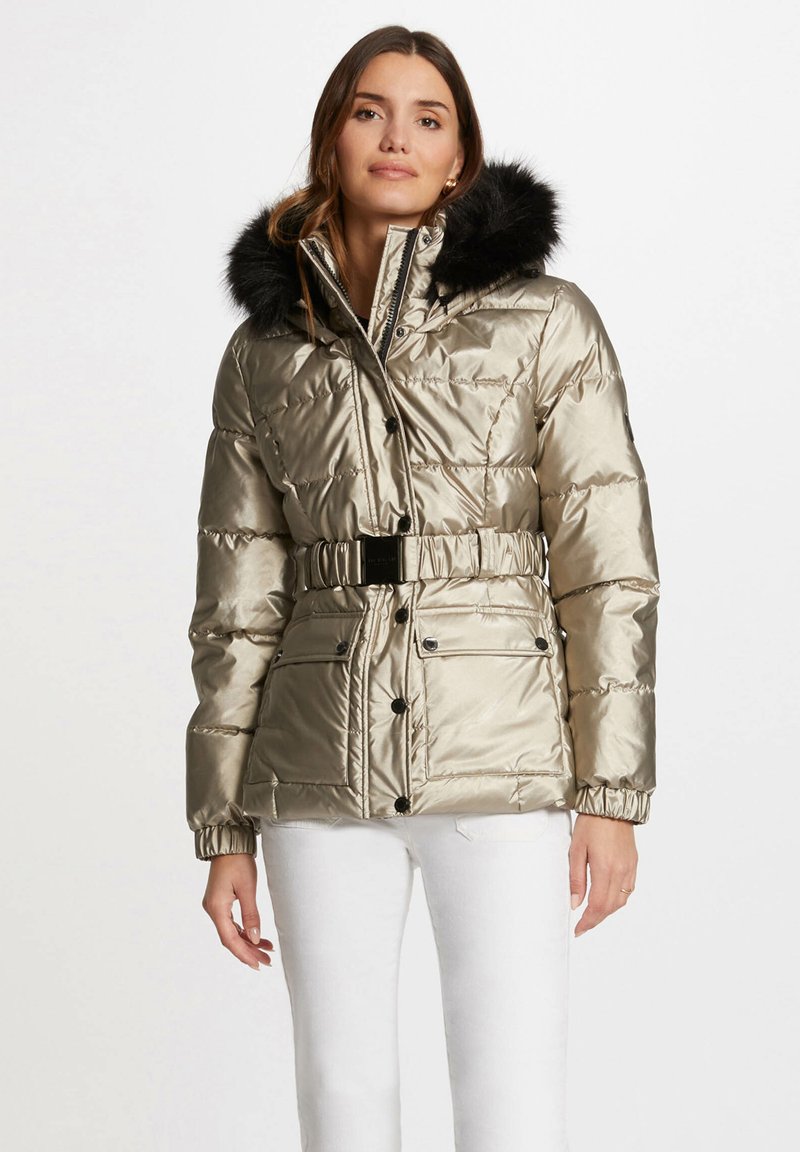 Veste dorée matelassée avec une capuche en fausse fourrure noire, taille cintrée et fermetures à pressions. Comprend deux poches avant et des poignets froncés.
