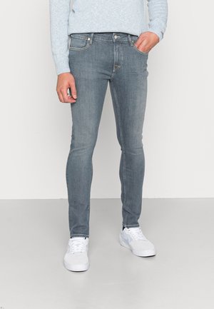 Jeans de ajuste slim, de denim azul claro con diseño de cinco bolsillos, ligero desgaste y costuras en contraste, combinados con zapatillas blancas.