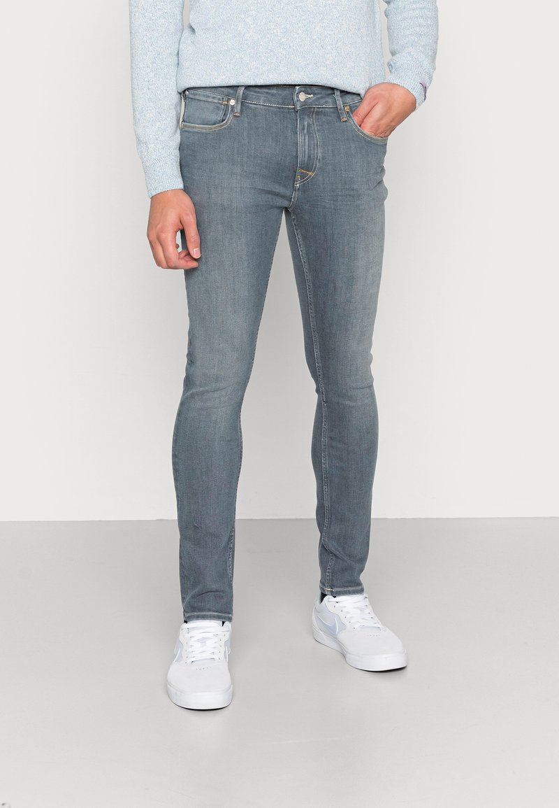 Jeans de ajuste slim, de denim azul claro con diseño de cinco bolsillos, ligero desgaste y costuras en contraste, combinados con zapatillas blancas.
