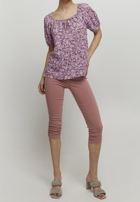 Blusa floral morada con mangas cortas acampanadas, combinada con leggings capri rosa y sandalias de tacón beige con acentos arrugados.