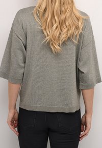 Metallisk sølv kortærmet sweater med løs pasform, rund halsudskæring, ribbet kant og tekstureret strikkemønster. Bæres med mørke jeans.