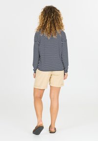 Marineblauw en witte gestreepte blouse met lange mouwen, gecombineerd met beige kniebroek. Vrouw staat met krullend haar en draagt tan sandalen.
