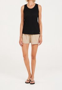 Czarny bezrękawnik z teksturowanej tkaniny i marszczonymi detalami na ramionach, w połączeniu z beżowymi szortami i czarnymi klapkami.