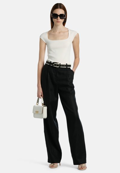 Top bianco aderente con scollatura quadrata, pantaloni neri a vita alta, cintura bicolore, occhiali da sole neri e piccola borsa bianca. Sandali testurizzati.
