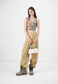 Débardeur multicolore court avec motif abstrait, pantalon cargo beige avec poches, bottines grises à la cheville et un petit sac à main blanc.