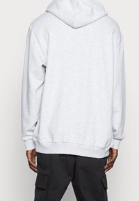 Ljusgrå bomullshuva med dragsnodd, oversized passform, ribbade muddar och fåll. Slät textur, inga ytterligare mönster eller accenter.