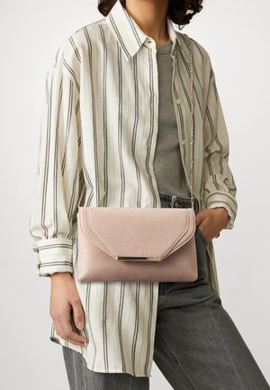 Persoon draagt een wit-zwart gestreept shirt en een grijze top, met een zachtroze envelopvormige clutch met een gouden metalen sluiting.