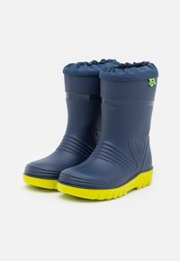 Bottes de pluie en caoutchouc bleu marine avec un design texturé, semelles jaunes vives et un bord froncé en haut. Présente un petit logo vert.