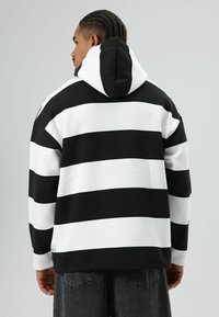 Hoodie rayé noir et blanc avec une grande capuche. Confectionné en tissu doux, il présente une coupe décontractée et des poignets côtelés. Étiquette de marque discrète à l'ourlet.