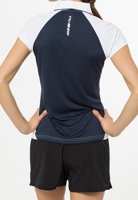 Mörkblå och vit kortärmad polo med hög krage och logotyp, kombinerad med svarta shorts. Tyget verkar slätt och figurnära.