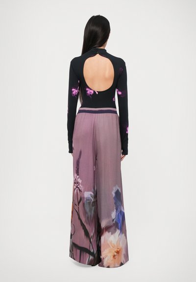 Black long-sleeve top with floral prints, back cutout, paired with wide-leg, pink floral-patterned trousers. Smooth fabric texture.