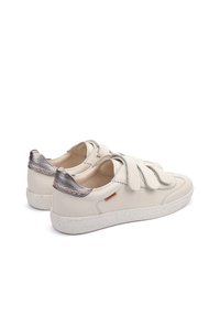 Zapatillas de piel blanca con un acento plateado texturizado en el talón. Presentan tres correas de velcro gruesas y una suela de goma moteada.