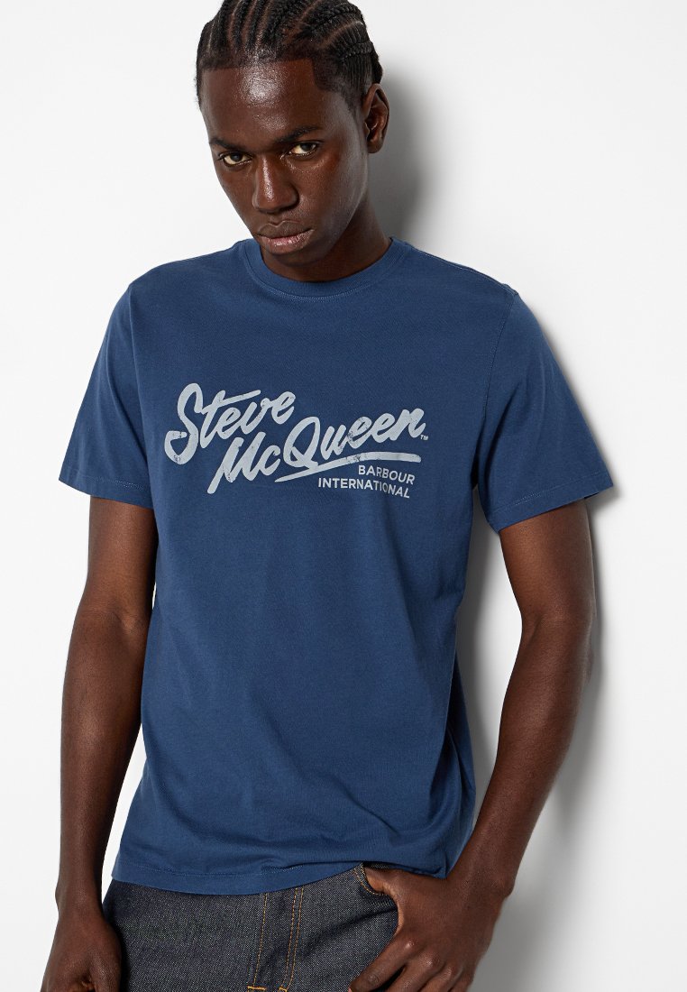 Camiseta de algodón azul marino con texto impreso en blanco que dice "Steve McQueen BARBOUR INTERNATIONAL." Con mangas cortas y un corte regular.