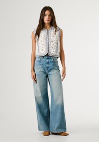 Prsluci s cvjetnim uzorkom u bijeloj boji, naglašeni ljubičastim rubom; uparen sa svijetloplavim, visokim širokim trapericama i bež cipelama.