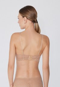 Bralette de encaje en color nude con tirantes ajustables, patrón floral y cierre de gancho en la parte posterior. Textura suave y semitranslúcida.