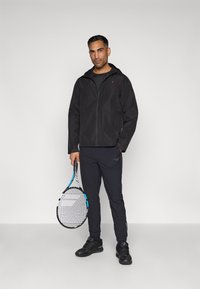 Must have veekindel must jope, millel on lukuga kapuuts ja esikotid, koos tumedate pükstega ja siniste aktsentidega tennisereketiga.