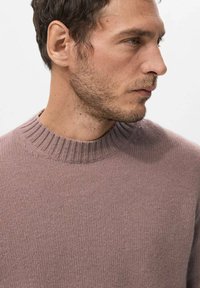 Jasnofioletowy sweter dziany z prążkowanym, okrągłym dekoltem, wykonany z teksturowanej tkaniny o dopasowanym kroju, noszony przez modelkę z krótkimi włosami.